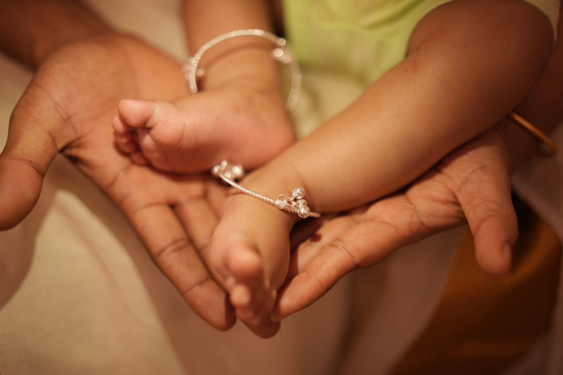 Baby feet with silver anklets held in parent's hands