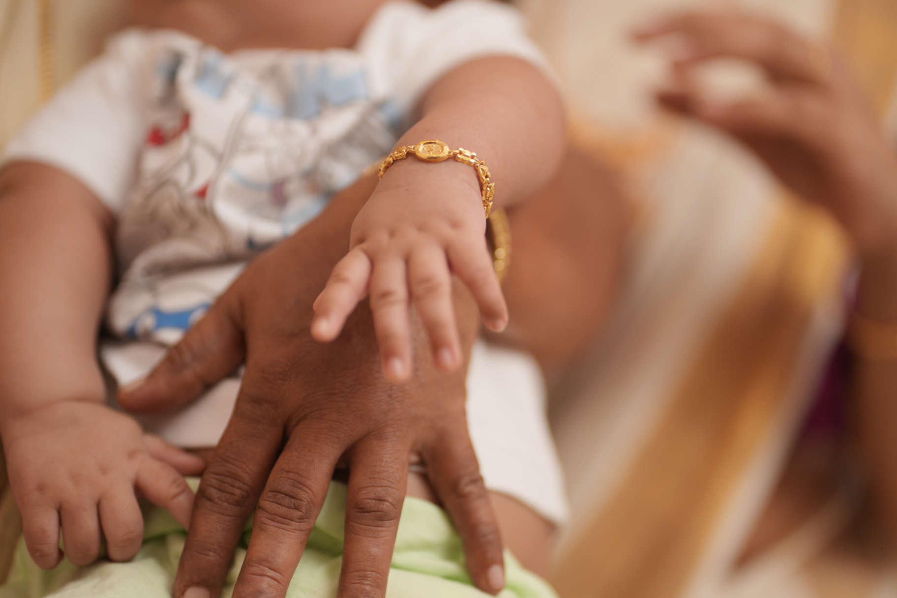Baby hand with gold bracelet resting on parent's hand